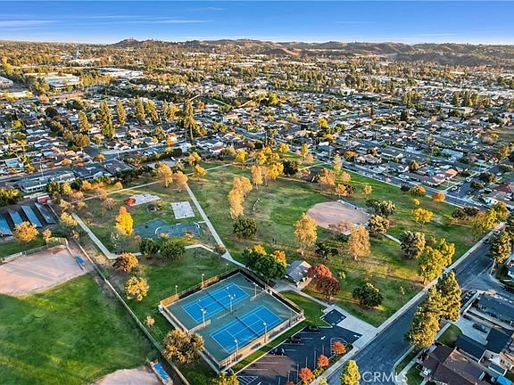 Aerial view of a vibrant park with sports fields, tennis courts, and a playground surrounded by lush trees in California